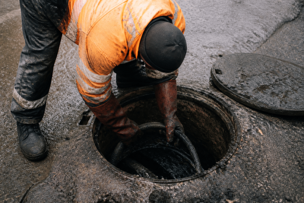 Ouvrier nettoie regard souterrain avec dépots accumulés visibles